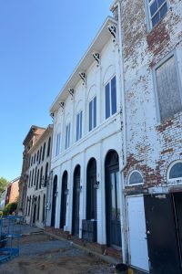 Historic white brick row of arched-entry storefronts with tall windows and decorative brackets under a clear blue sky; construction debris visible in foreground.