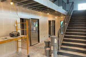 Construction area under renovation with scaffolding, buckets, and a metal staircase to the right; taped-off doorways and exposed wiring overhead.