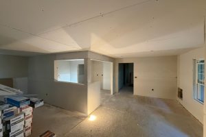 Unfinished interior with drywall partially installed; a small framed room has a large window opening and a doorway beyond, with construction boxes stacked to the left and scattered debris on the floor.