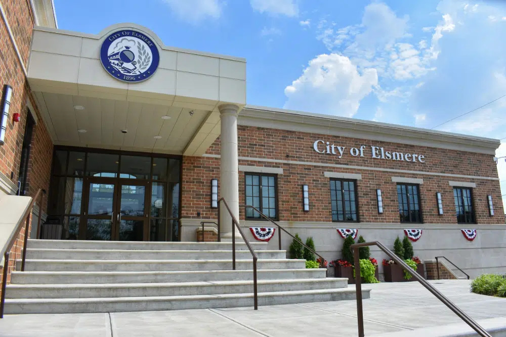 Large stone roadside sign reading 'City of Erlanger Kentucky' with a landscaped flower bed in front and a bright blue sky behind it