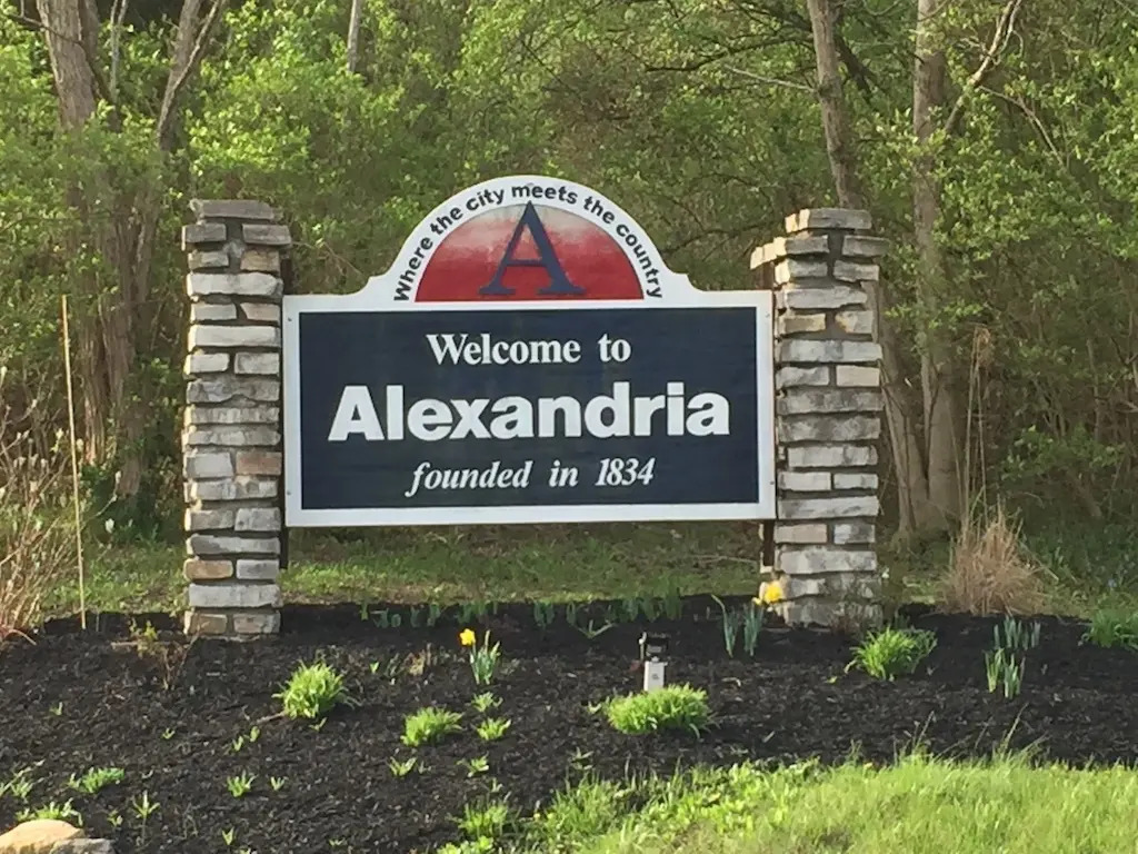 Large stone roadside sign reading 'City of Erlanger Kentucky' with a landscaped flower bed in front and a bright blue sky behind it