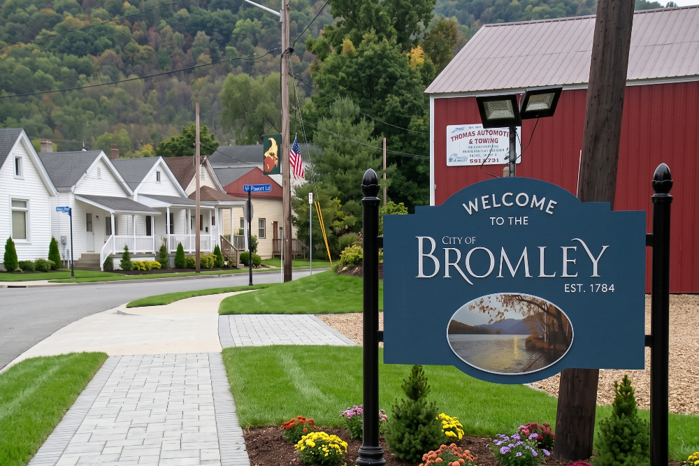 Large stone roadside sign reading 'City of Erlanger Kentucky' with a landscaped flower bed in front and a bright blue sky behind it