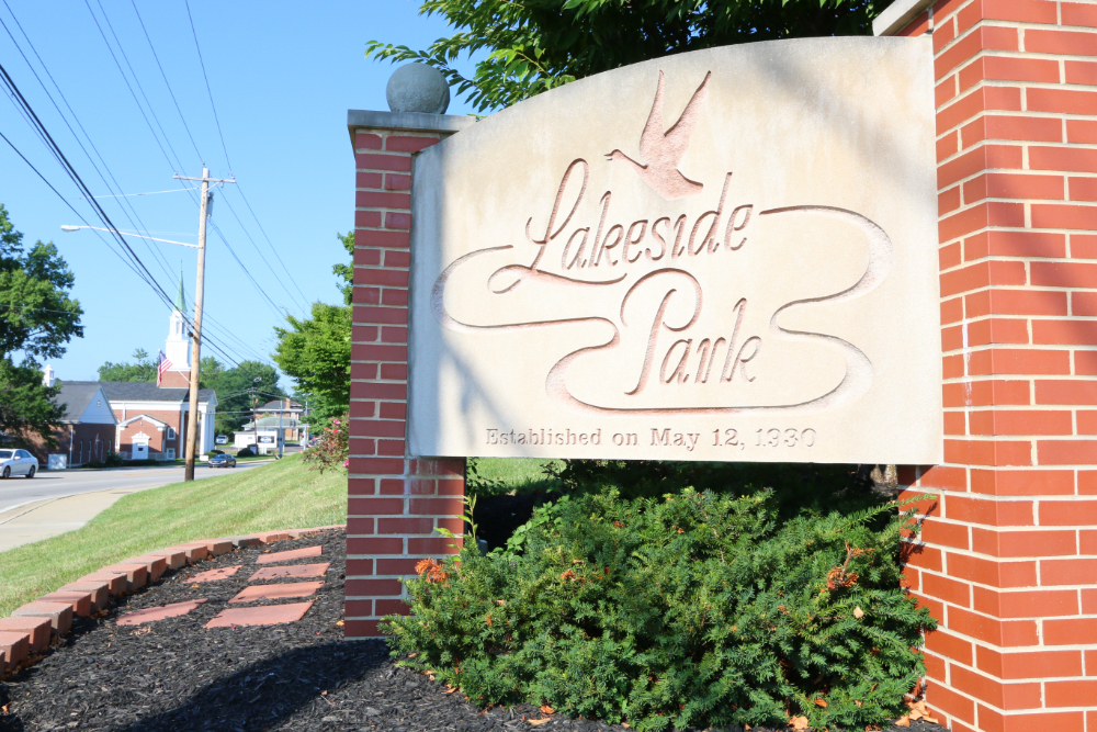 Large stone roadside sign reading 'City of Erlanger Kentucky' with a landscaped flower bed in front and a bright blue sky behind it
