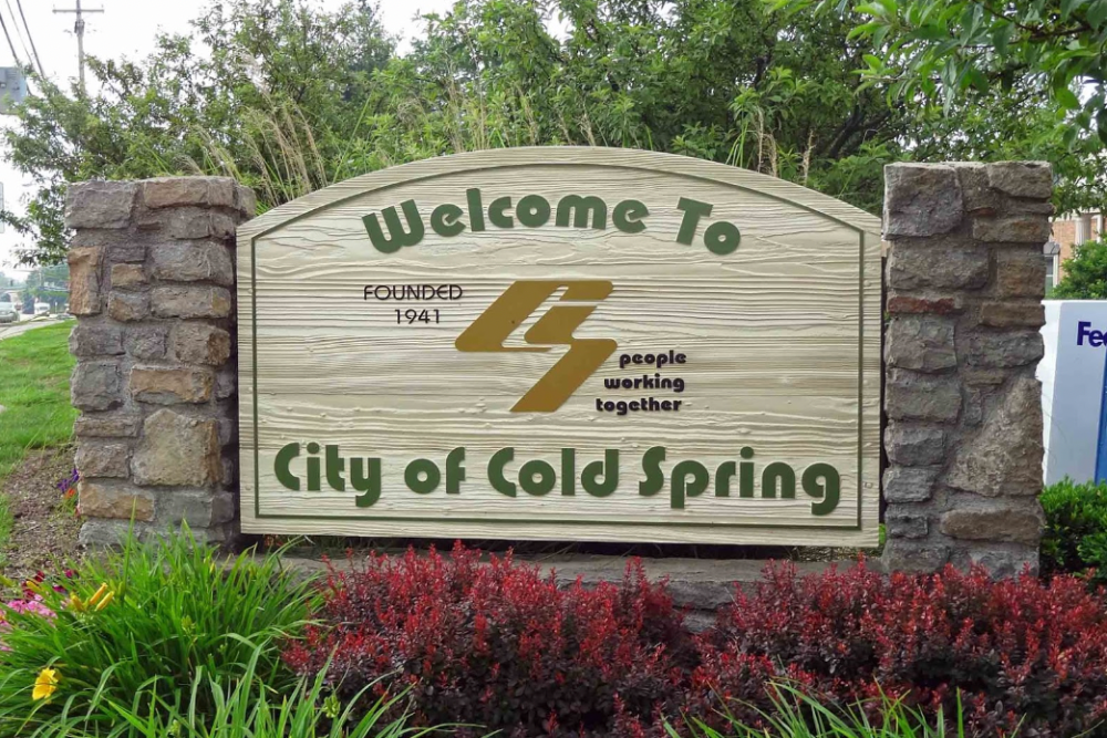 Large stone roadside sign reading 'City of Erlanger Kentucky' with a landscaped flower bed in front and a bright blue sky behind it