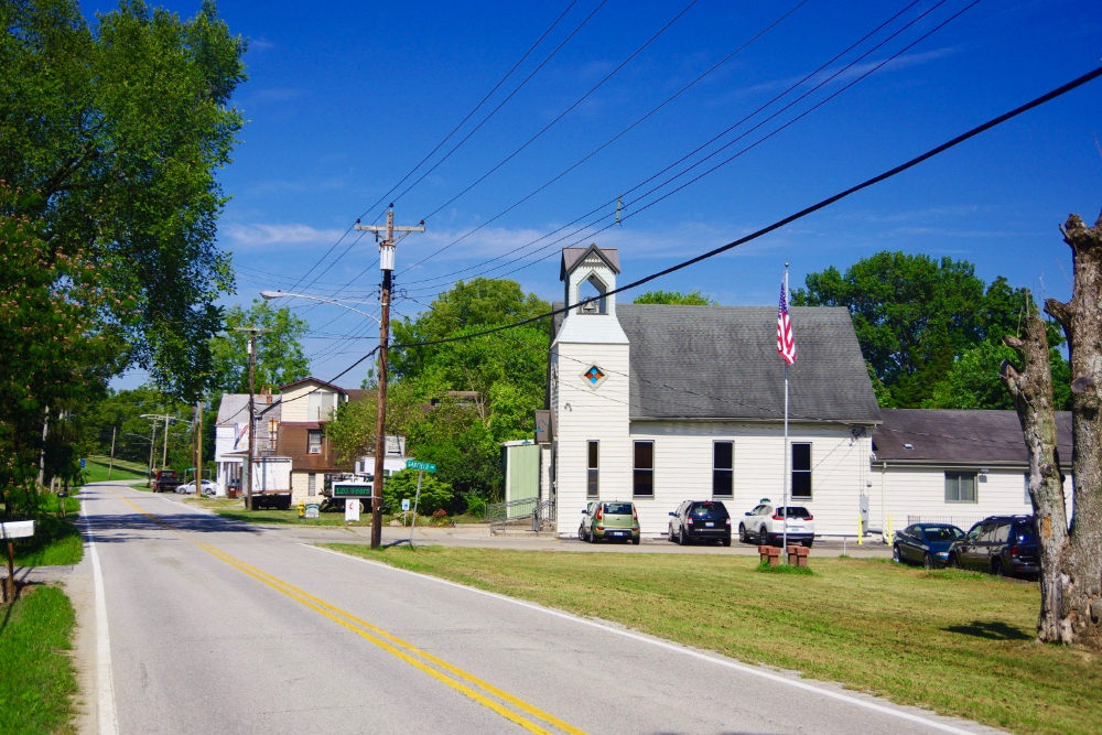 Large stone roadside sign reading 'City of Erlanger Kentucky' with a landscaped flower bed in front and a bright blue sky behind it